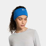 A woman wearing a bright blue athletic headband with a white logo, paired with a light gray long-sleeve top, photographed against a clean light gray studio background.