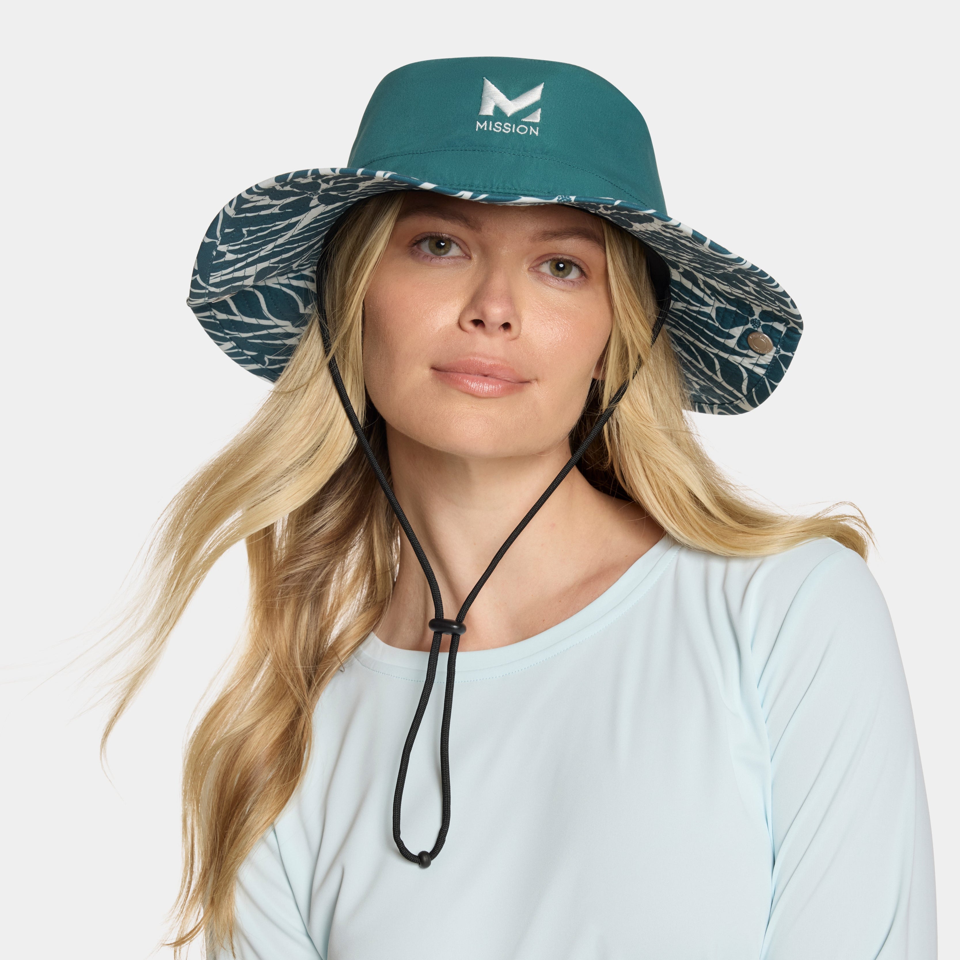 Woman wearing a teal sun hat with a patterned brim on a white background