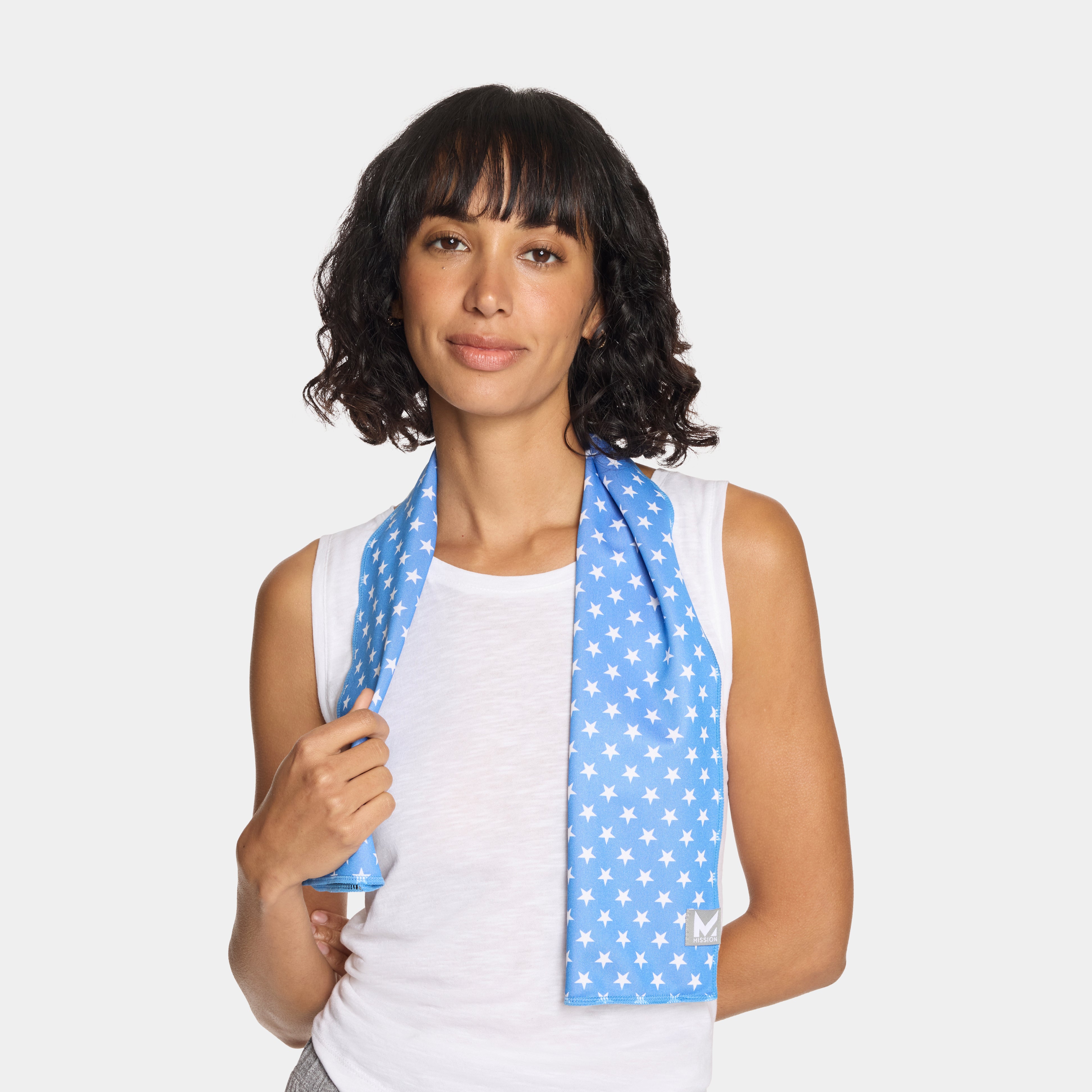 A woman with dark curly hair wearing a white tank top and a light blue athletic scarf with a white star pattern, posed against a solid light gray background.