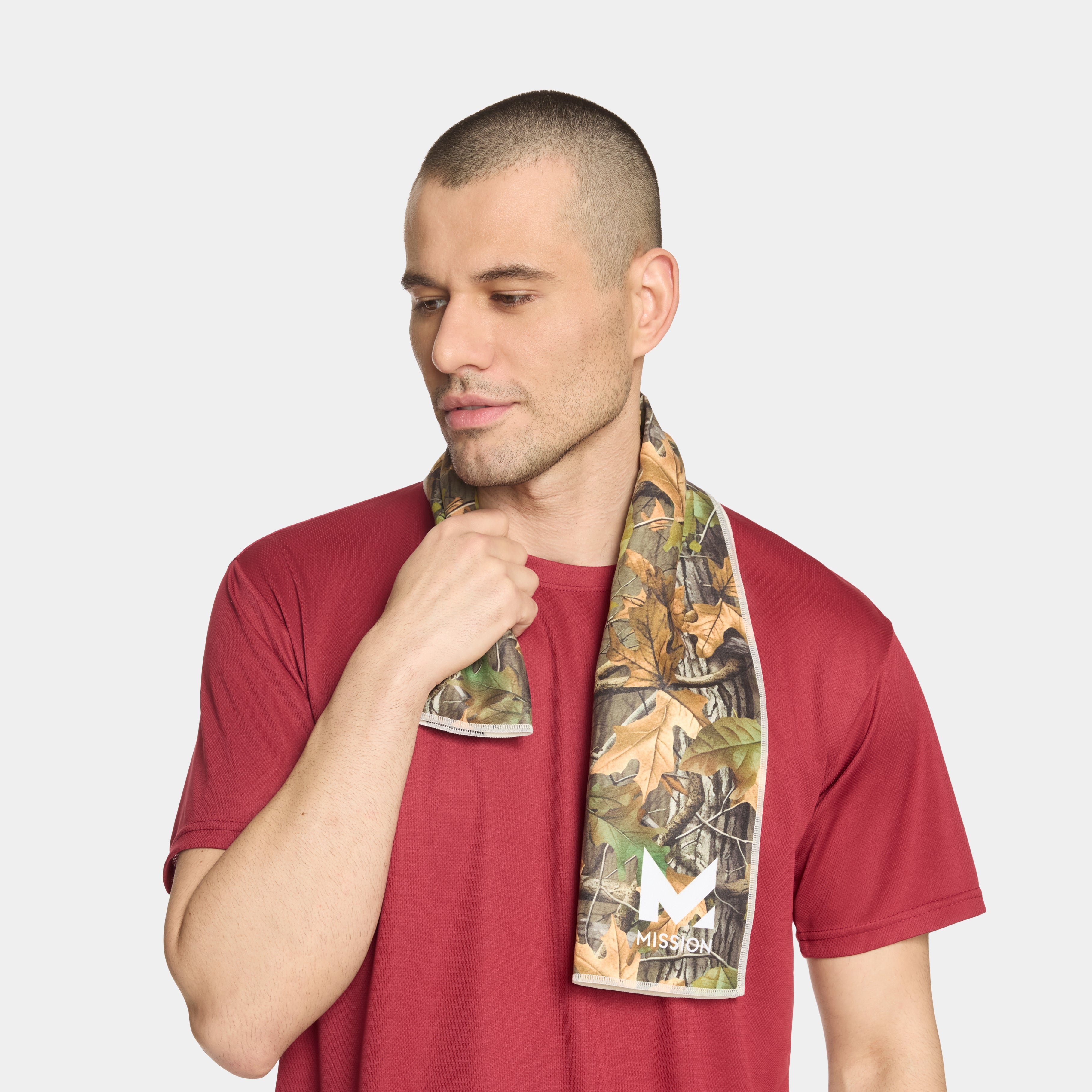 A man wearing a red t-shirt and a camouflage neck gaiter with a Mission brand logo, set against a plain light gray background.