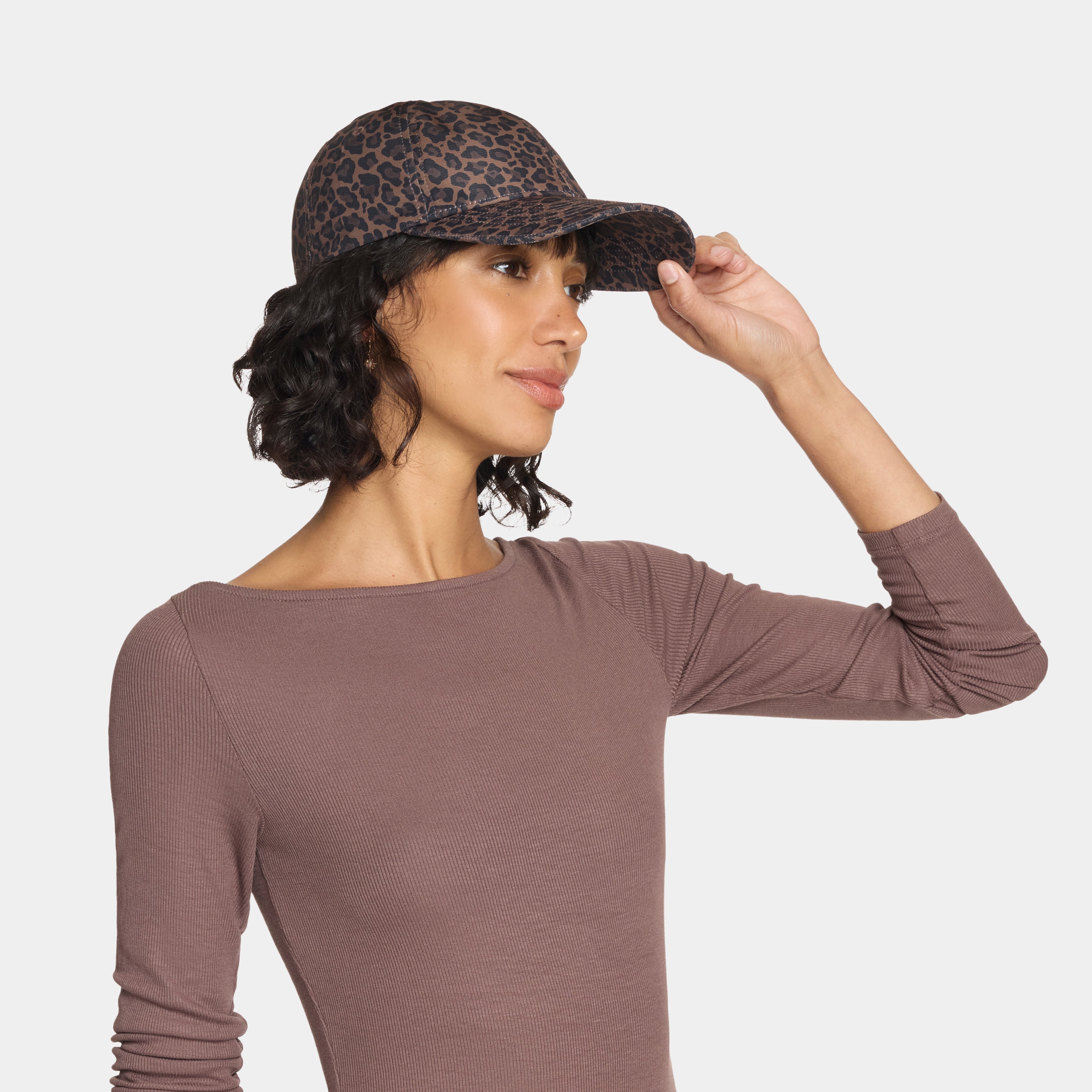 Woman wearing a brown long-sleeve top and a leopard print cap on a white background